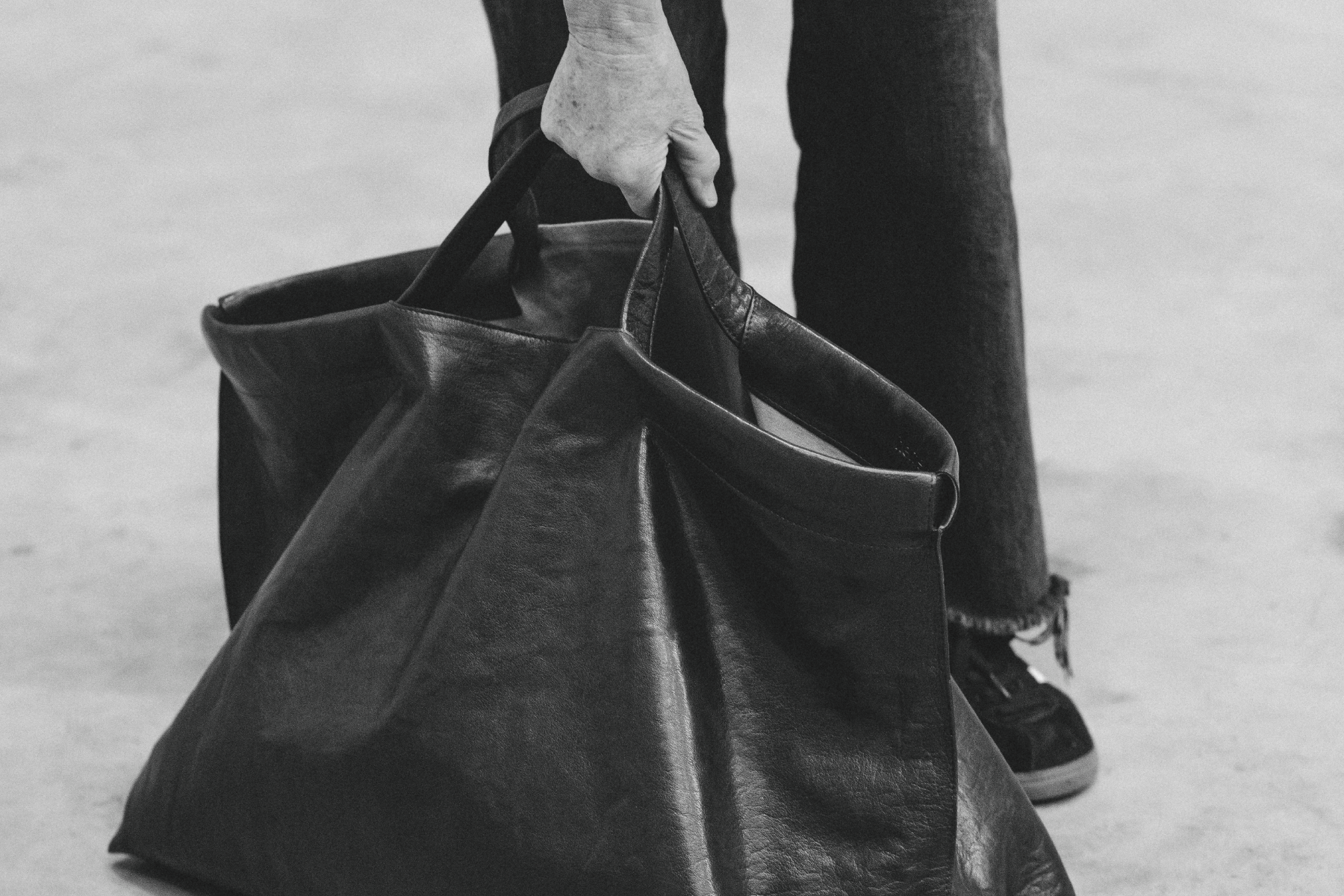A person placing a black leather bag on the ground.